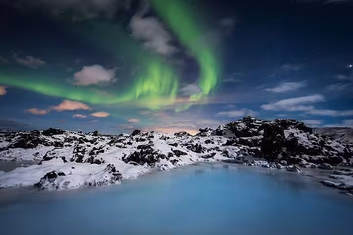 Aurora borealis glowing green over Blue Lagoon geothermal spa surrounded by snow-covered lava fields in Iceland