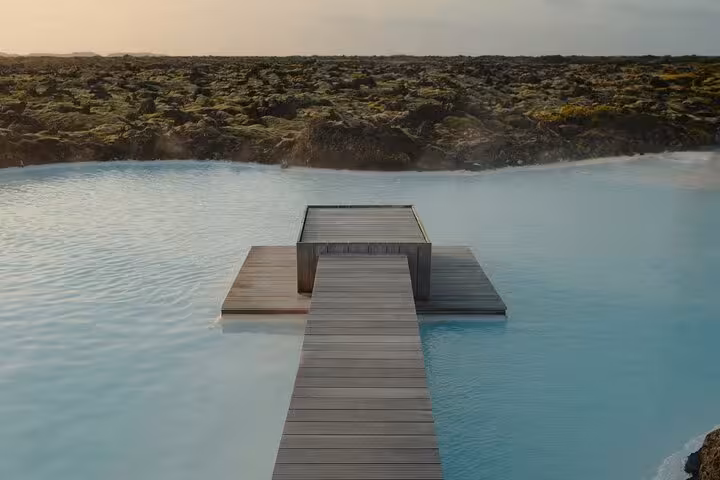 Wooden dock extending into milky blue geothermal waters of Blue Lagoon Iceland with lava fields beyond