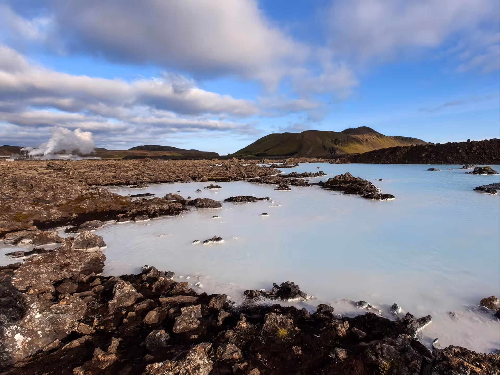 Milky blue geothermal waters of Blue Lagoon Iceland with volcanic lava rocks and steam rising in background