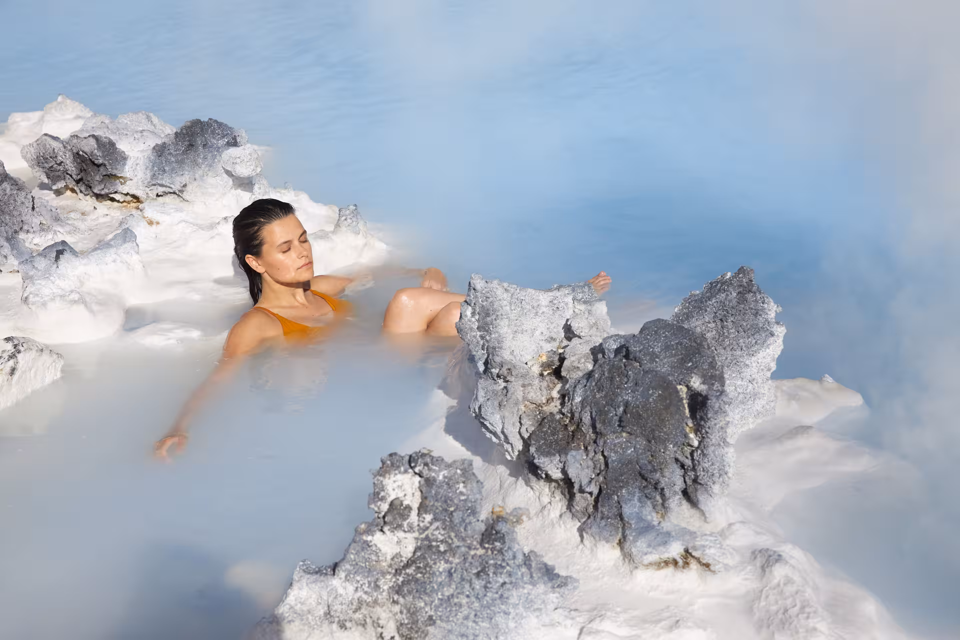 Woman relaxing in the warm, mineral-rich waters of Iceland's Blue Lagoon, surrounded by natural lava rocks.