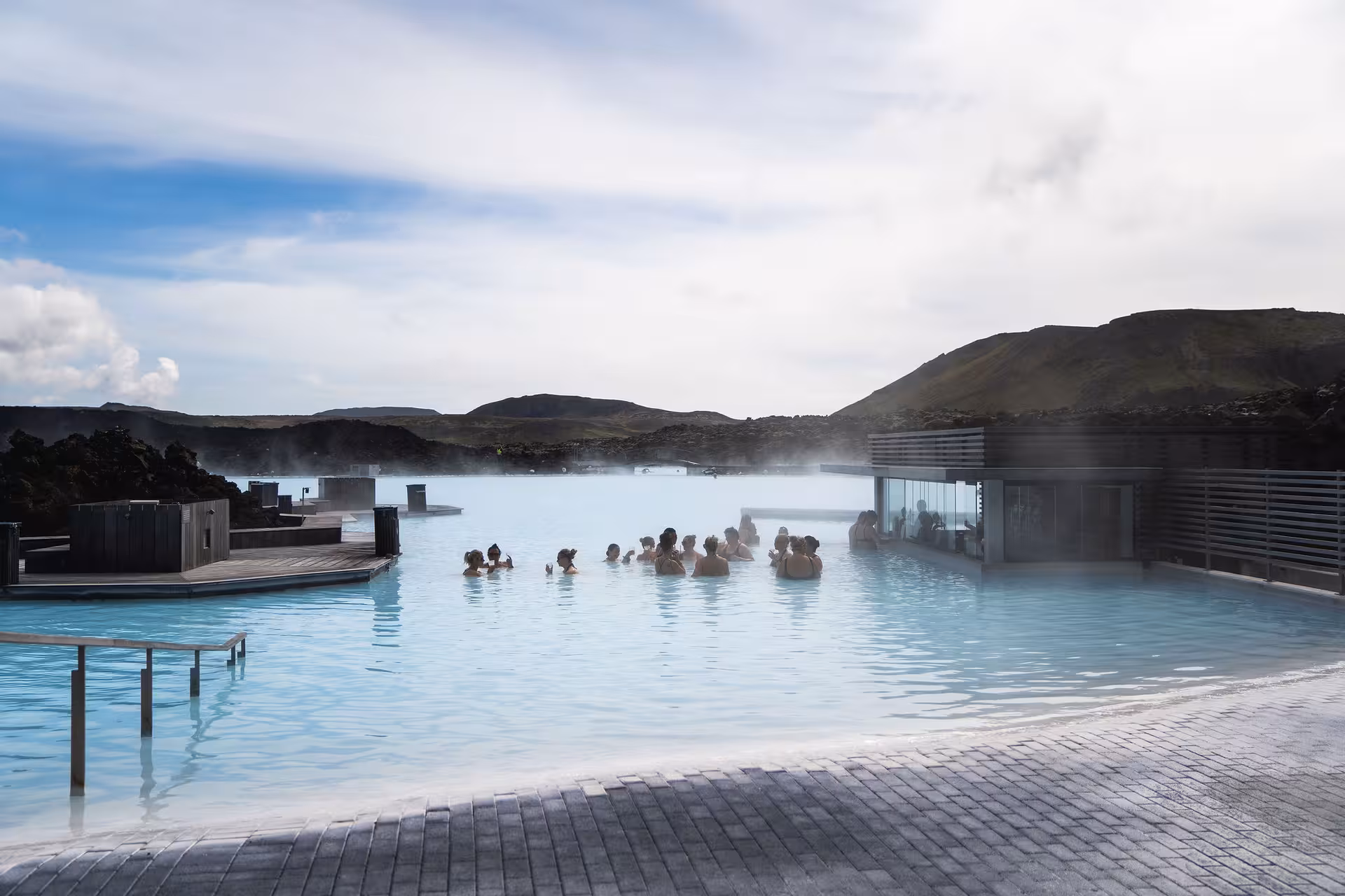 Visitors soaking in the milky blue geothermal waters of the Blue Lagoon with steaming hot springs and volcanic hills