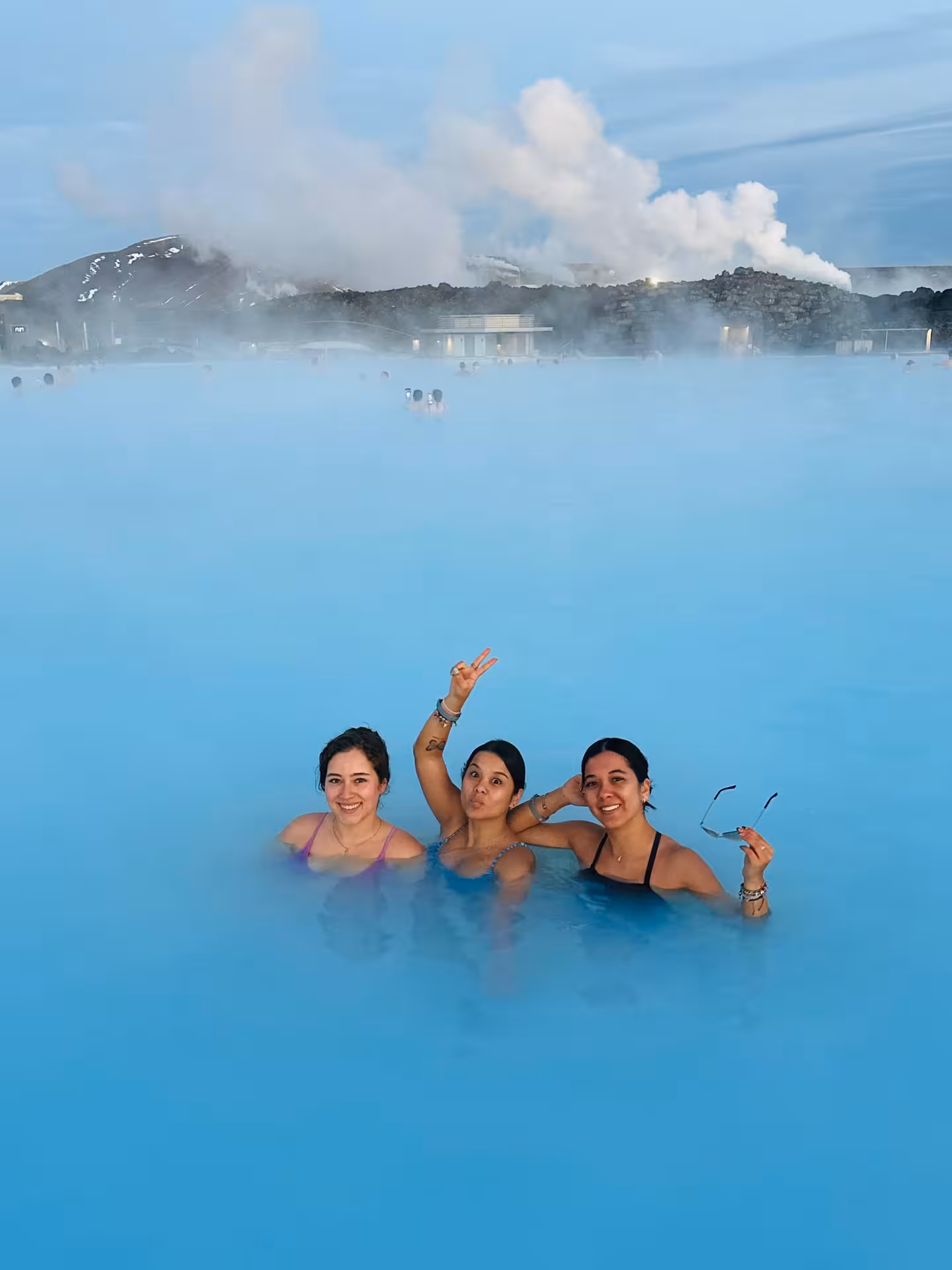 Three women smiling in the milky blue geothermal waters of the Blue Lagoon Iceland with steam rising