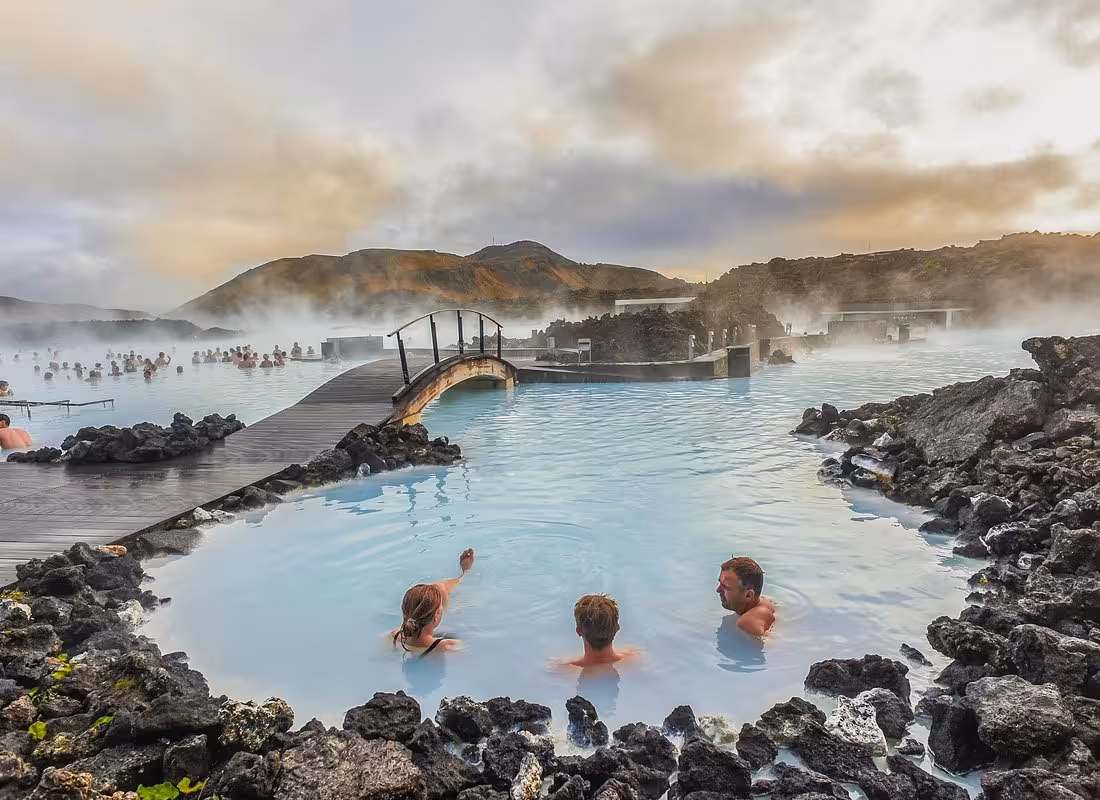 Visitors soaking in the milky blue geothermal waters of Blue Lagoon Iceland surrounded by lava rocks and steam