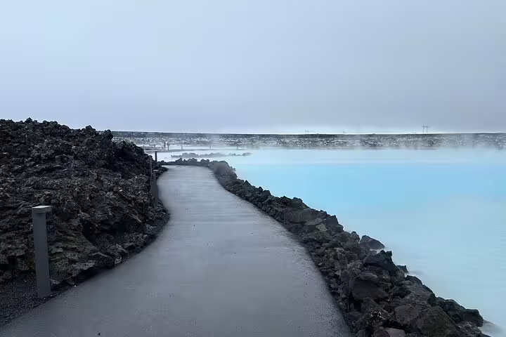 Steaming blue geothermal waters of Blue Lagoon Iceland with black lava rock pathway on overcast day