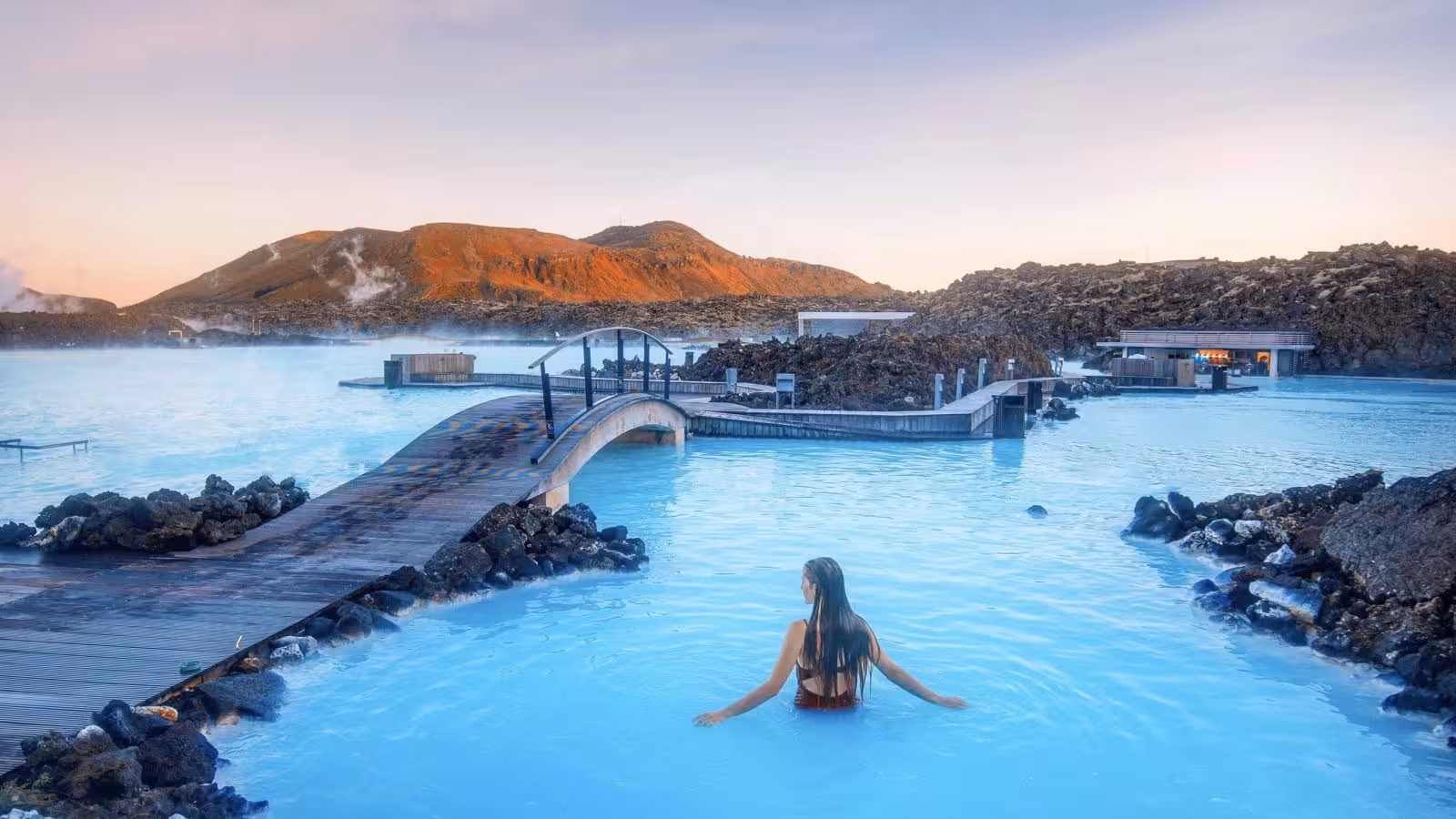 Traveler soaking in Iceland Blue Lagoon with lava rocks and footbridge, classic Blue Lagoon to Reykjavik tour