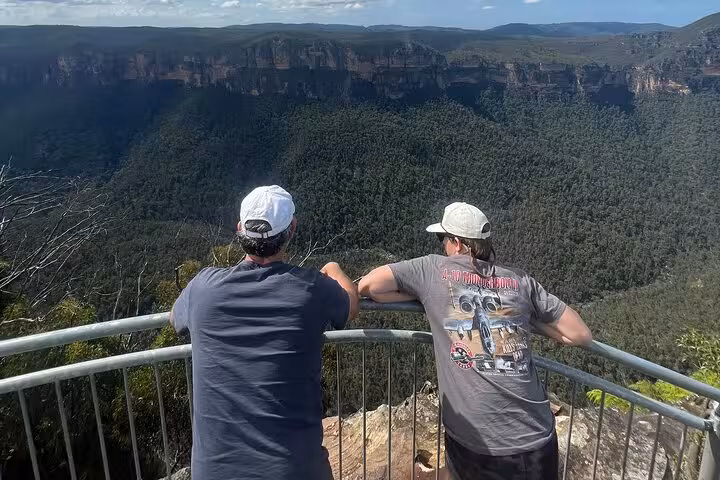 Two visitors enjoying panoramic views of the Blue Mountains from a lookout on a private tour with pickup and drop-off.