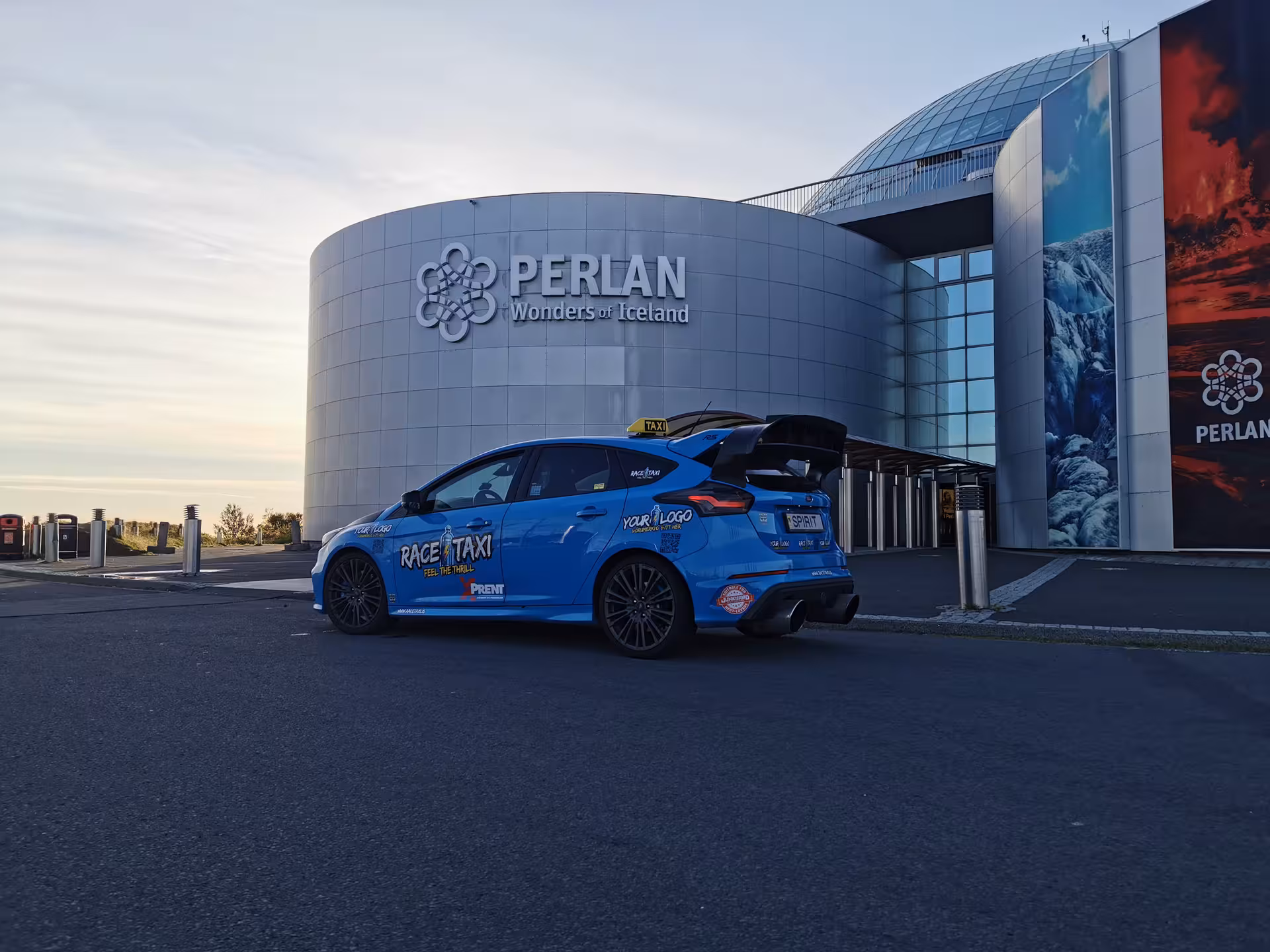 Blue rally car taxi outside Perlan Reykjavik, private Iceland airport transfer with race-inspired ride