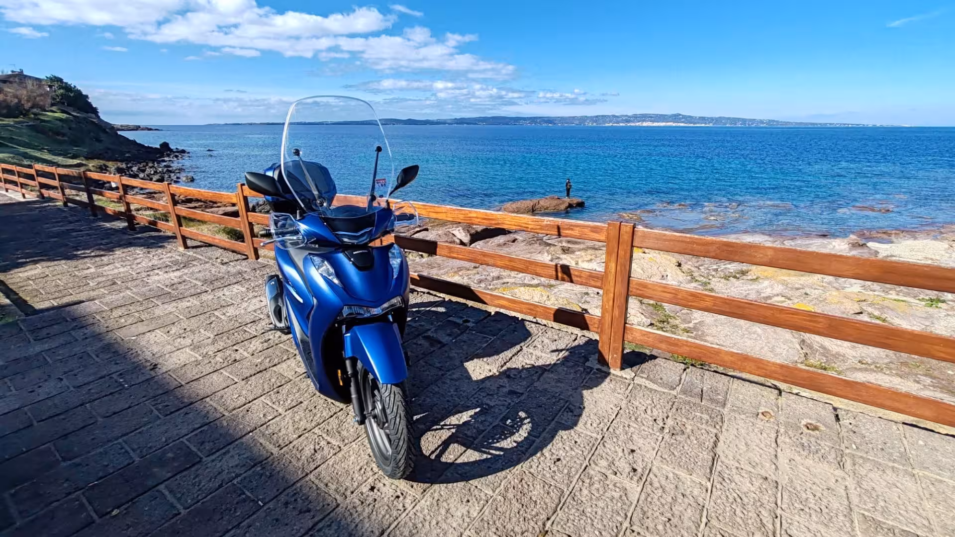 Blue scooter parked by scenic seaside in Calasetta, ideal for exploring coastal views and local attractions.