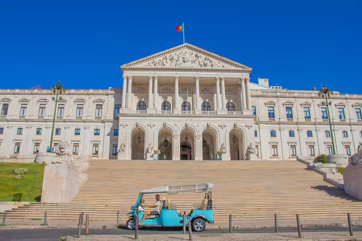 Blue TukTuk in front of Lisbon's São Bento Palace during a private tour with a local guide, showcasing historic architecture.