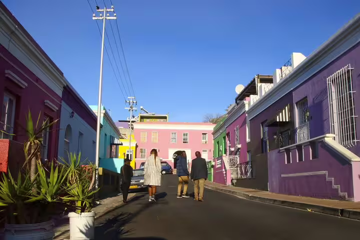 Tourists walking in Bo-Kaap, Cape Town, surrounded by brightly painted houses on a sunny day.