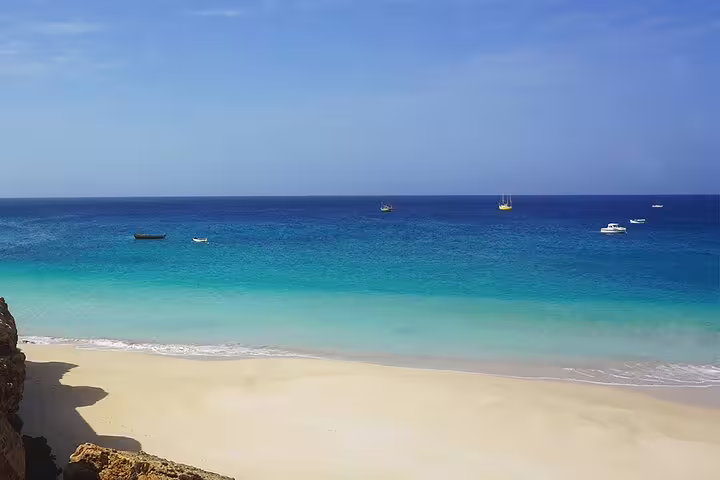 Serene sandy beach with clear turquoise waters and boats in the distance on Boa Vista Island, perfect for relaxation.