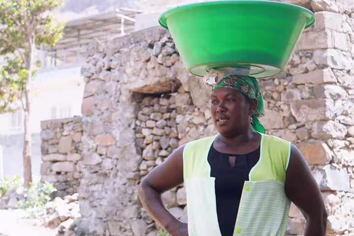 Local woman balancing a green basin on her head, representing vibrant cultural scenes on Boa Vista Island.