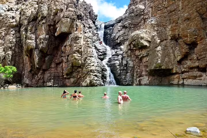 Visitors enjoying a swim in a natural pool beneath a majestic waterfall on Boa Vista Island, ideal for adventure tours.
