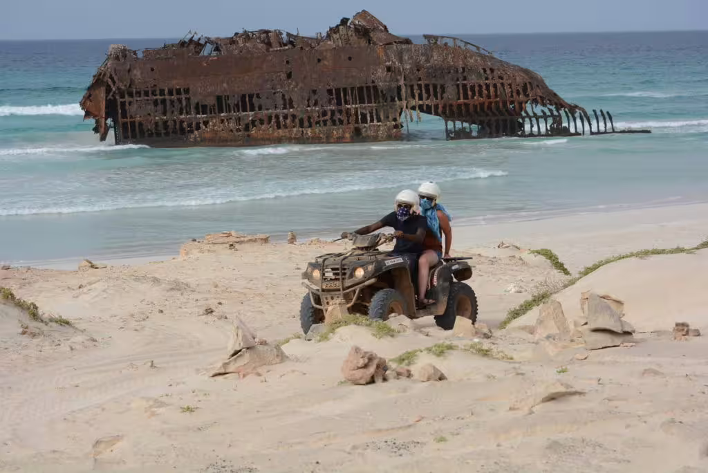 Adventurers on a quad bike explore Boa Vista's sandy shores with the iconic Cabo Santa Maria shipwreck in the background.