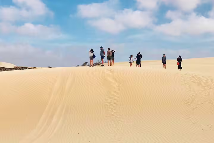 Visitors walking on golden sand dunes under a bright blue sky on Boa Vista Island, Cape Verde.
