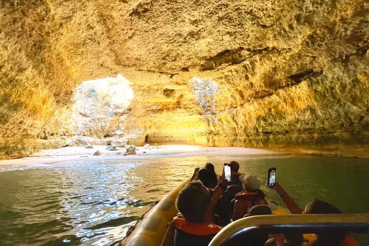 Boat entering Benagil Cave grotto, passengers filming golden rock walls on Algarve private charter cruise