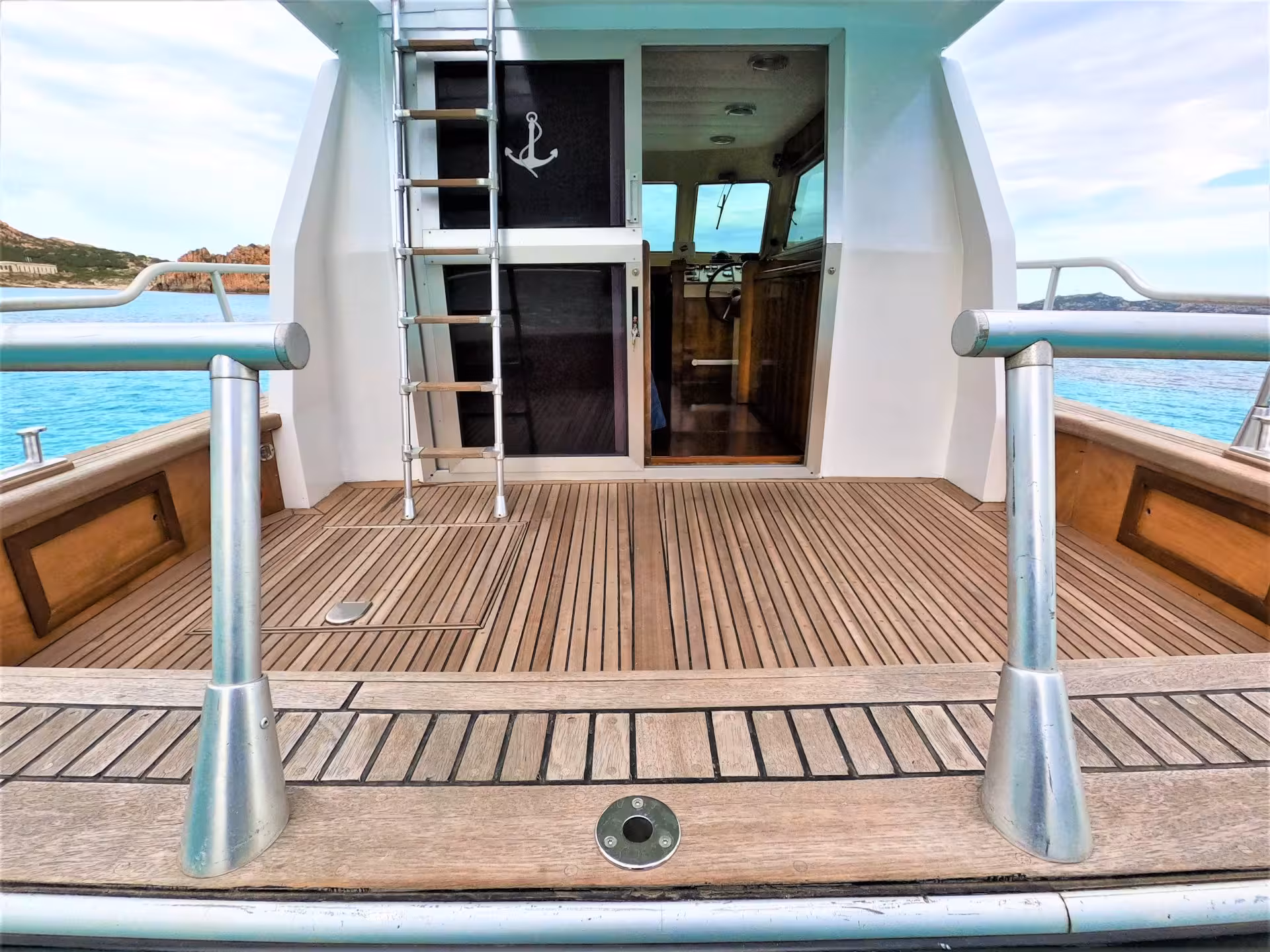 Interior view of a boat with wooden deck and ladder, cruising through the scenic waters of La Maddalena Archipelago.