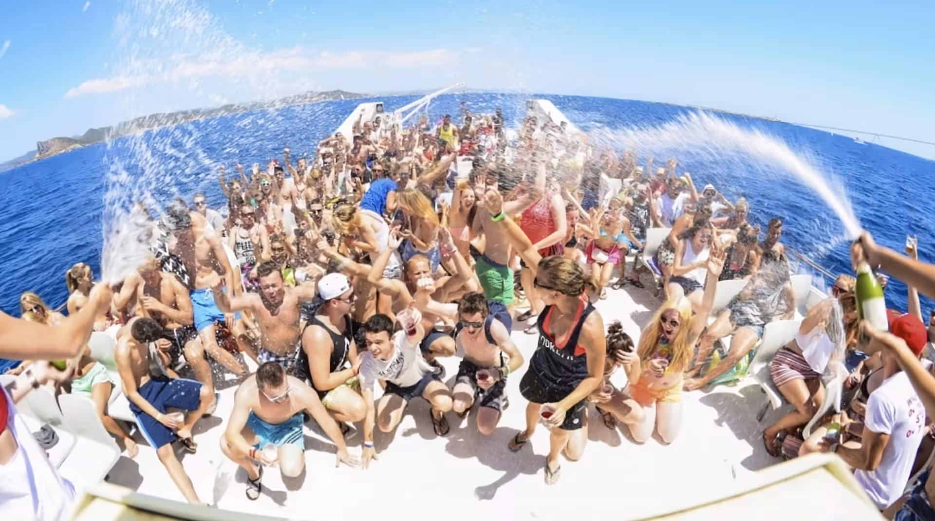 Large group of tourists partying on a boat deck in Cannes, spraying champagne under sunny blue skies