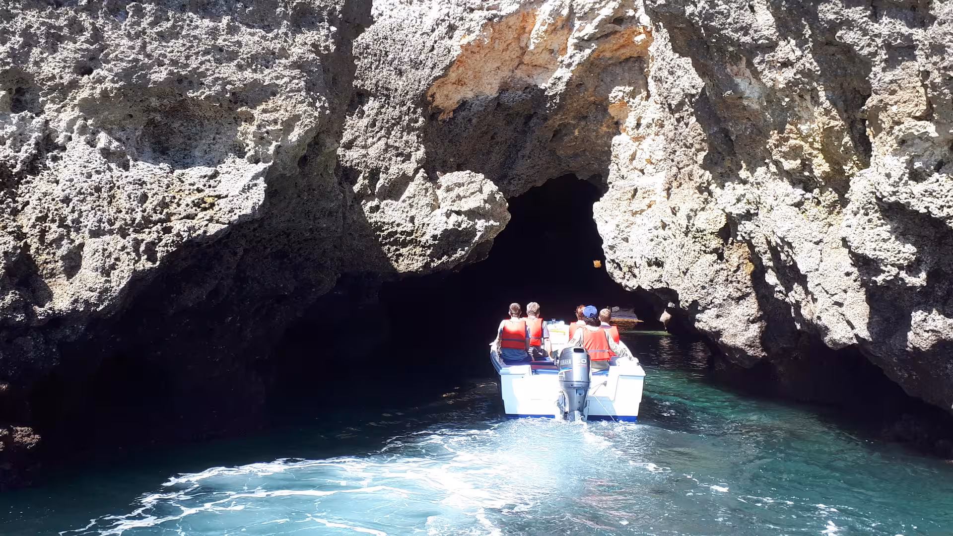 Small tour boat entering a dramatic sea cave at Ponta da Piedade, Lagos, on a guided Algarve coastline cruise