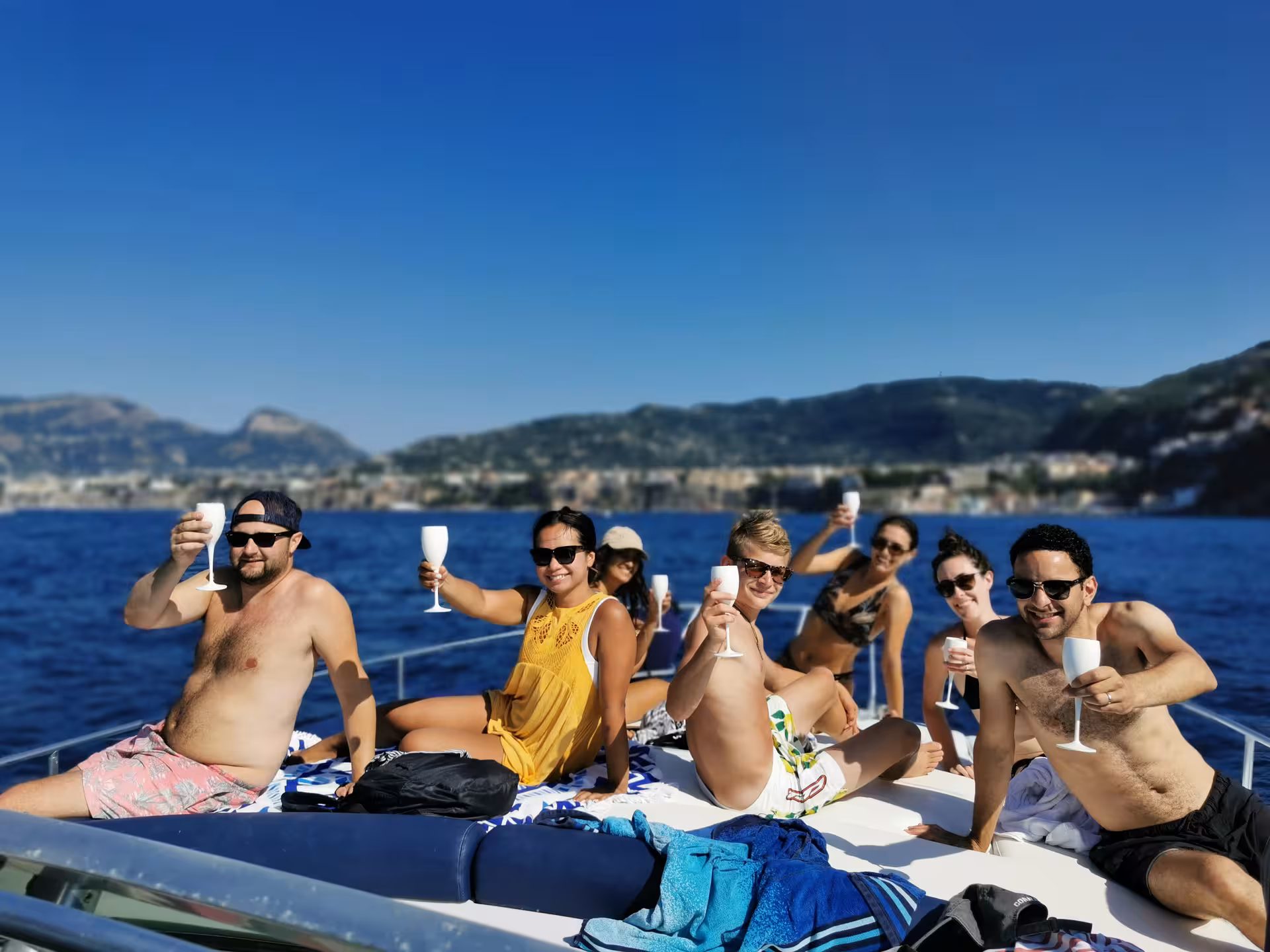 Group of joyful tourists enjoying drinks on a sunny boat tour to Amalfi and Positano from Sorrento.