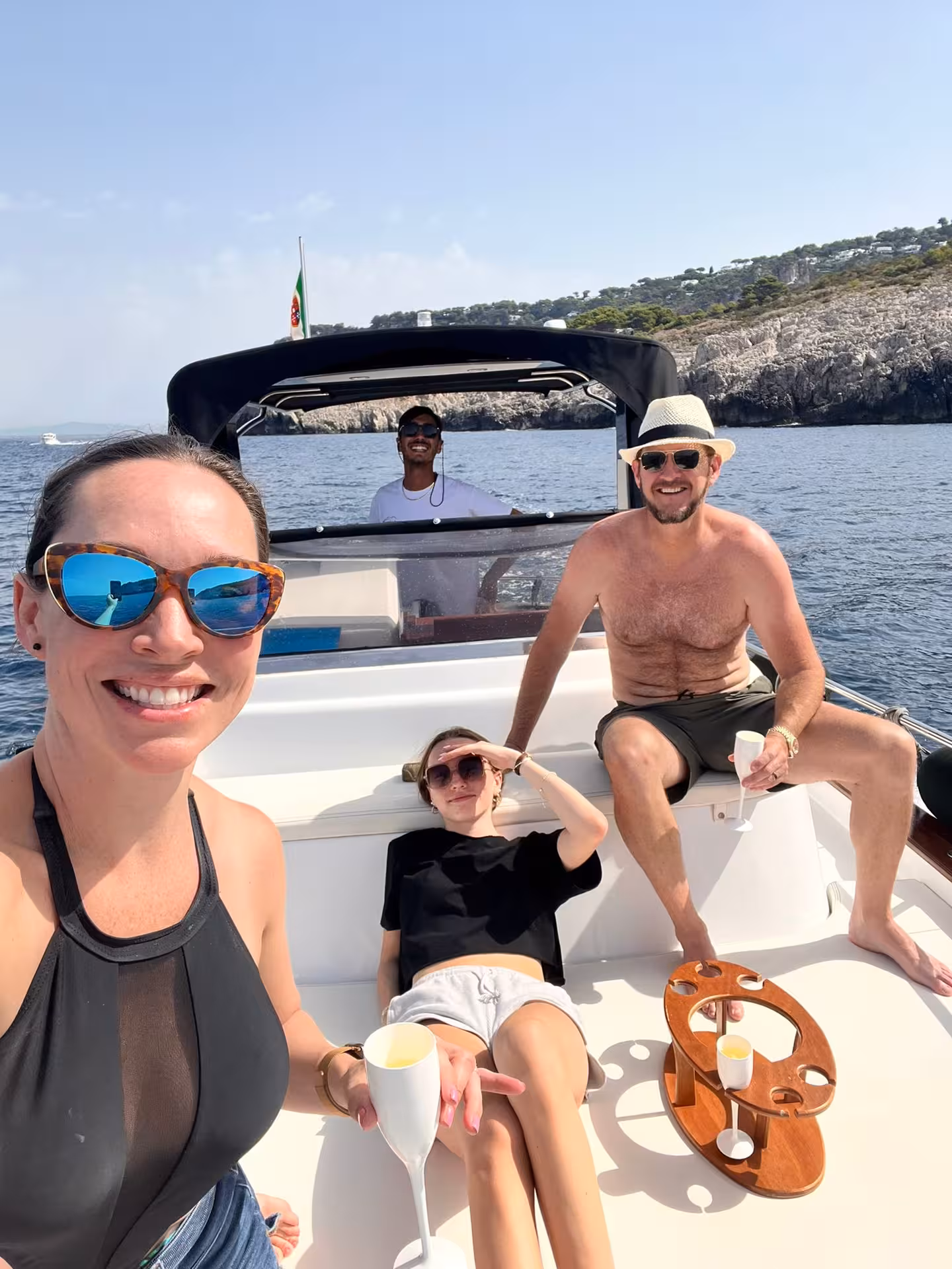 Group of friends enjoying a relaxing boat tour to Capri, lounging with drinks against a backdrop of cliffs.