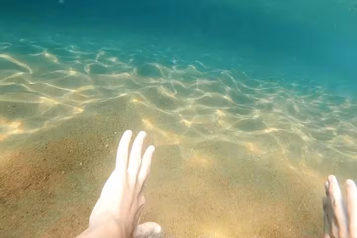 Hands reaching towards the sandy ocean floor in pristine waters on a captivating boat excursion.