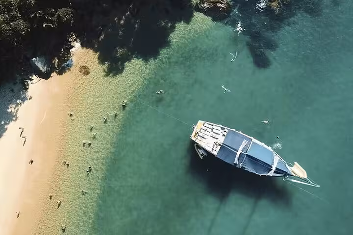 Aerial view of a boat anchored near a scenic beach with swimmers enjoying the clear turquoise waters on a Paraty tour.