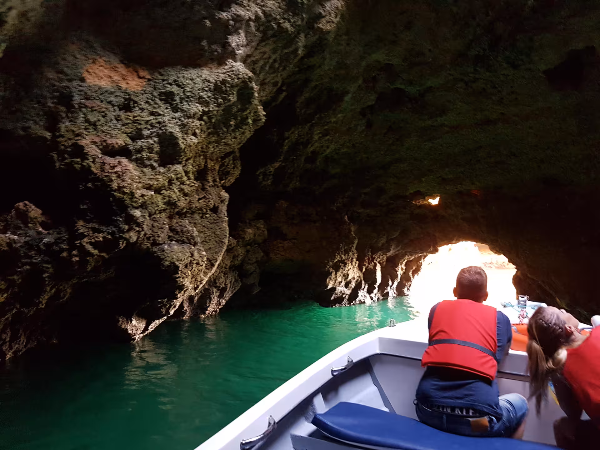 Visitors in life jackets on a Lagos grotto tour glide by boat through the dark Ponta da Piedade caves toward a sunlit opening