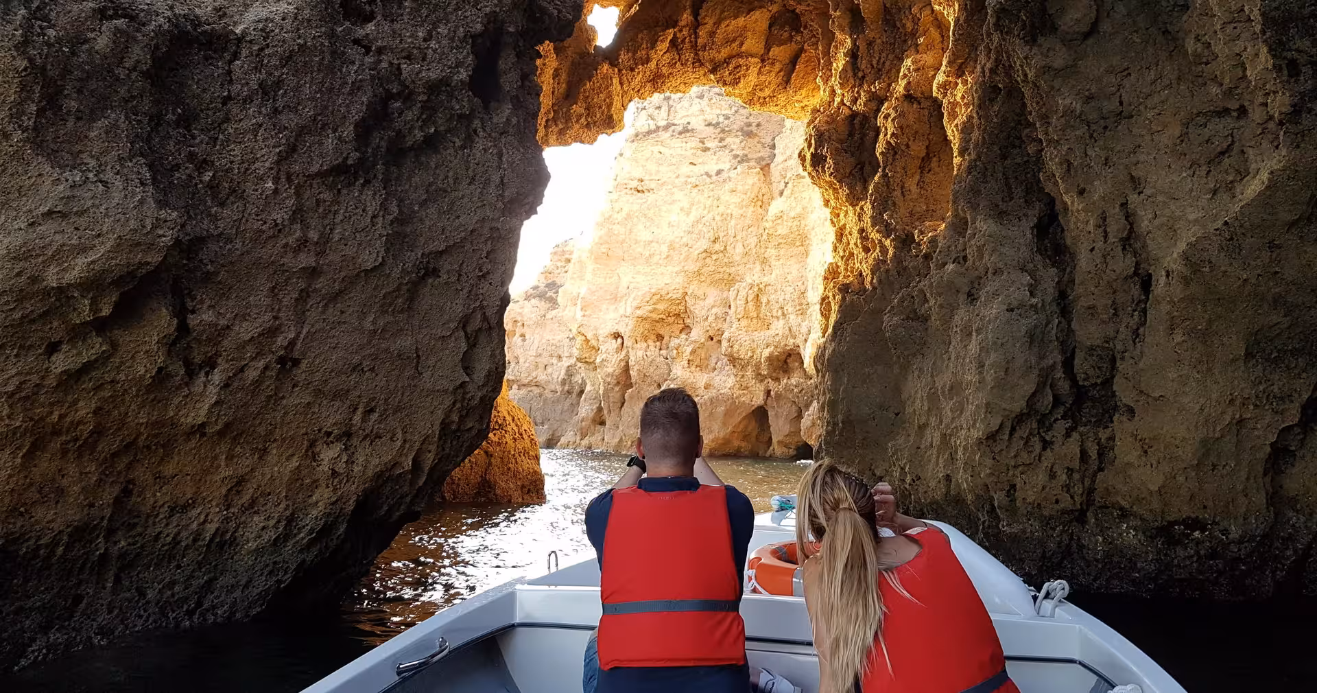 Couple on guided boat tour entering golden Ponta da Piedade sea caves in Lagos, exploring dramatic Algarve coastline.