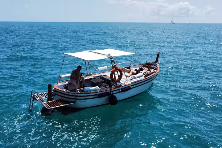 Side view of a covered boat with people lounging as it sails smoothly in the blue waters near Portovenere.