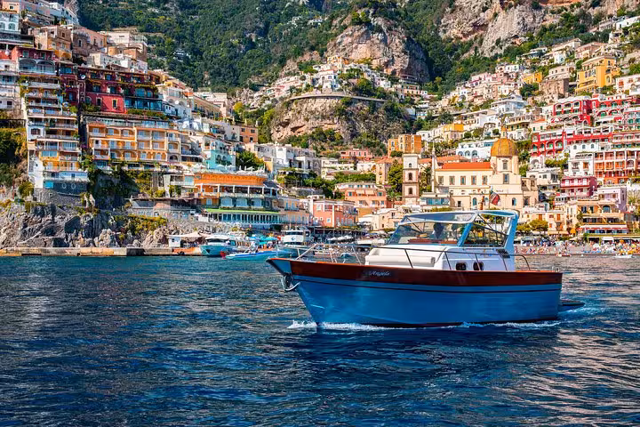 Boat cruising along the vibrant coastline of Positano with colorful cliffside buildings in the background.