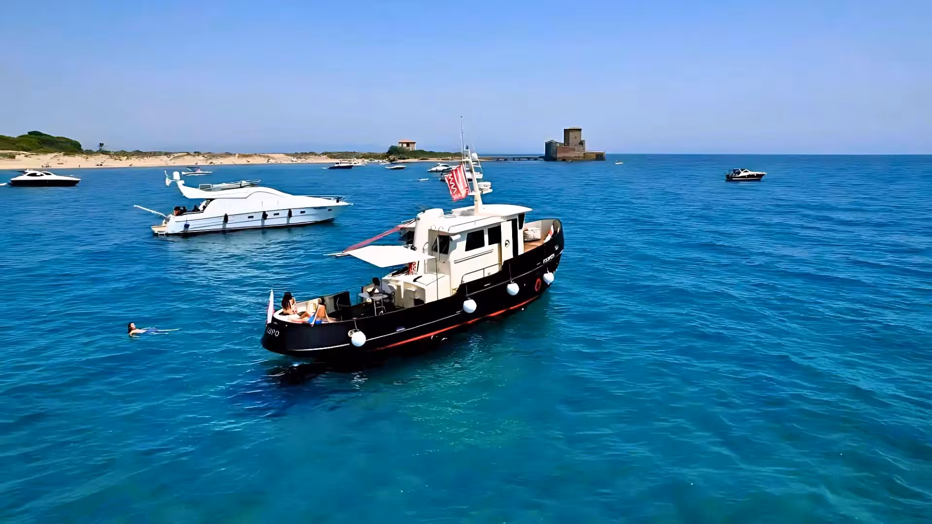 Relaxing boat excursion with yachts and swimmers in Molara's turquoise waters, showcasing Sardinia's coastal beauty.