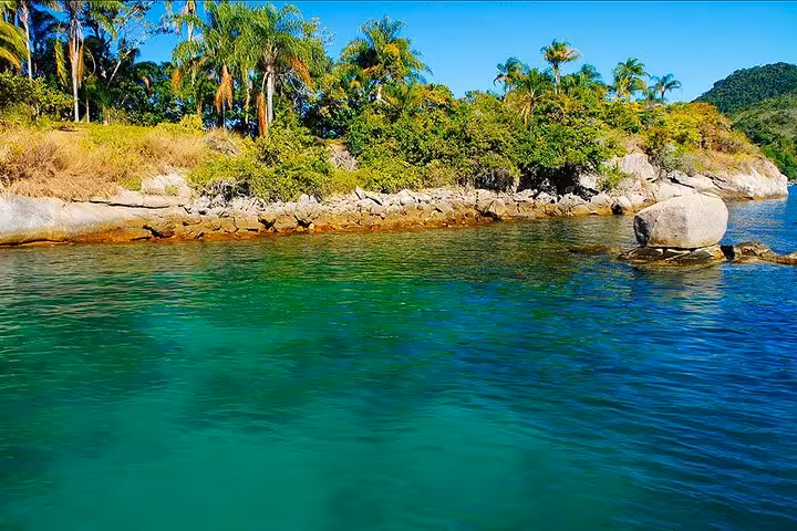Vibrant turquoise waters and rocky shoreline with tropical vegetation, offering a picturesque view on a boat tour adventure.