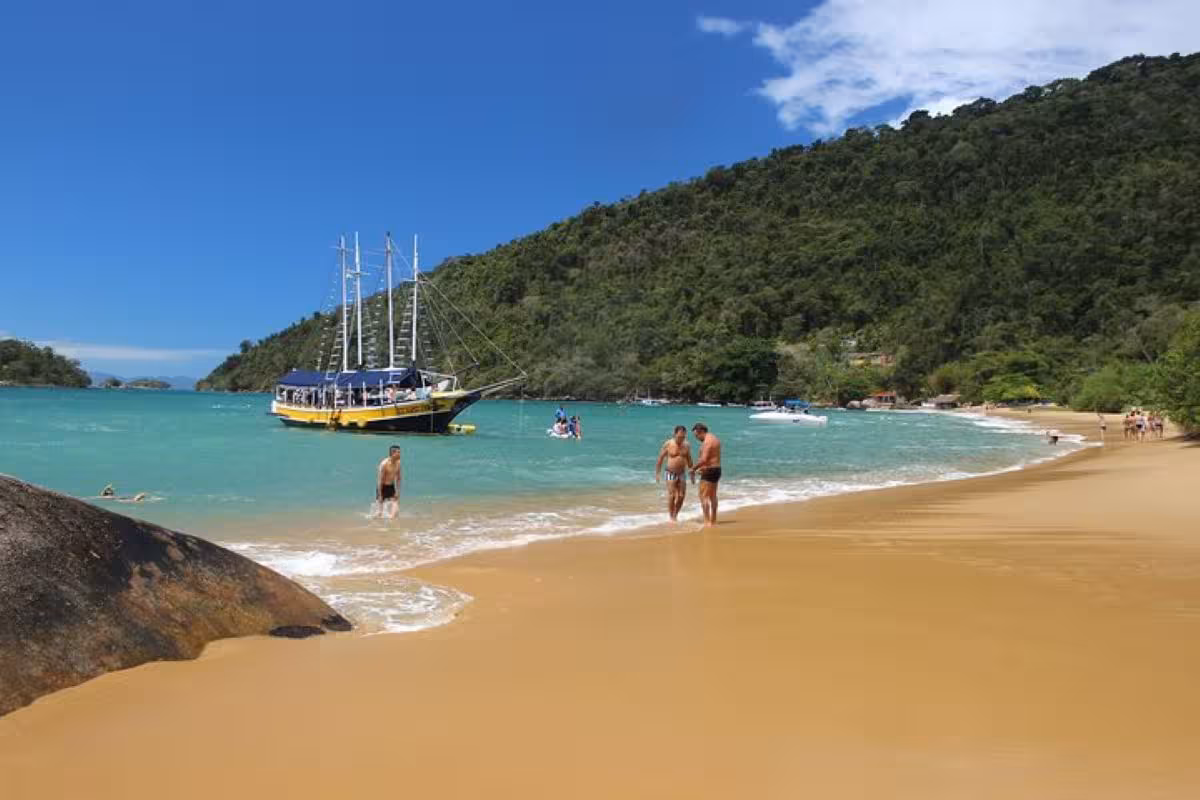 Serene beach with people enjoying the water and a boat anchored nearby on a sunny day.