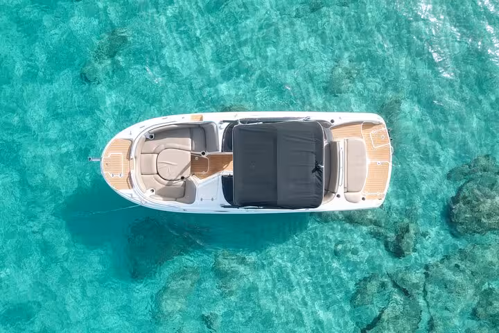 Top view of a sleek boat anchored on turquoise waters, highlighting the serene beauty of Cala Bassa and Cala Comte tour experience.