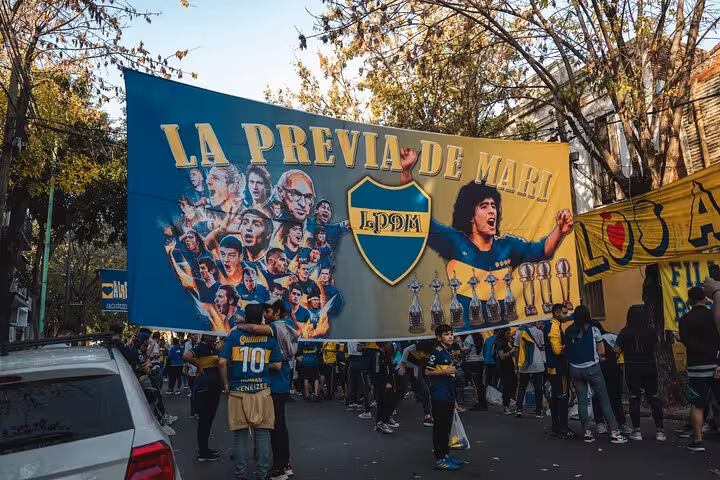 Boca Juniors fans holding La Previa de Maradona banner near La Bombonera, pre-match local tour with transport in Buenos Aires