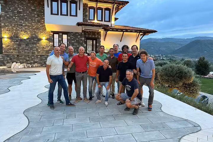 A group of friends pose happily in front of a picturesque villa with mountains in the background during a waterfall adventure tour.