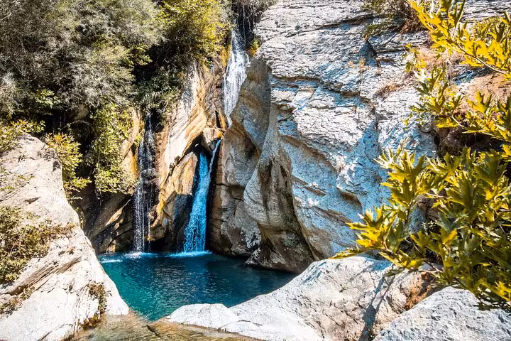 Stunning waterfall cascades into a turquoise pool surrounded by rocky cliffs and lush greenery on Bogove's Splendor tour.