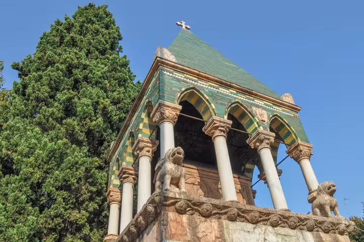 Ornate medieval tower with green tiled roof, stone lion sculptures, arched columns, and a cross in Bologna