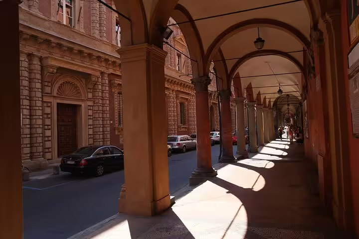 Historic portico walkway in central Bologna, with arches, warm sunlight and Renaissance palaces on a private guided tour route