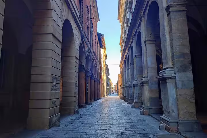 Narrow cobblestone street lined with arched stone porticoes in Bologna's historic old town