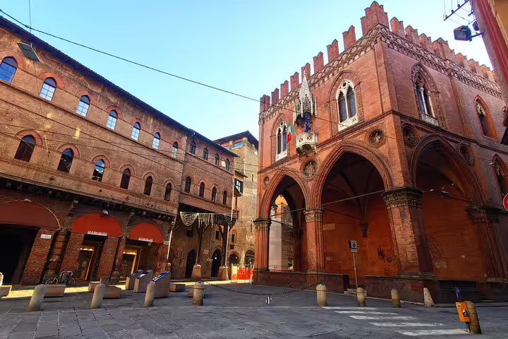 Medieval red brick buildings and Gothic arcades in Bologna's historic Old Town piazza under blue sky