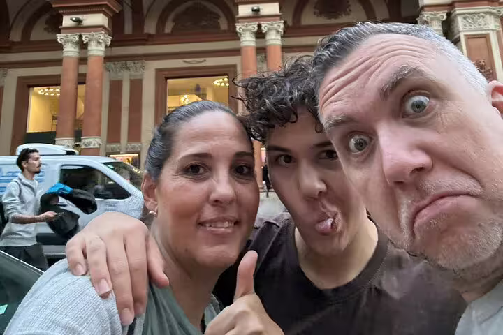 Three tourists taking a fun selfie in front of a historic Bologna building during a walking tour