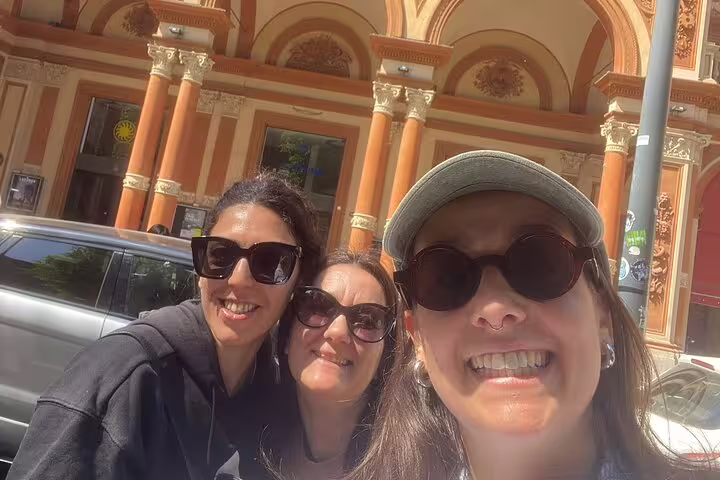 Three smiling women taking a selfie in front of a grand historic building in Bologna old town