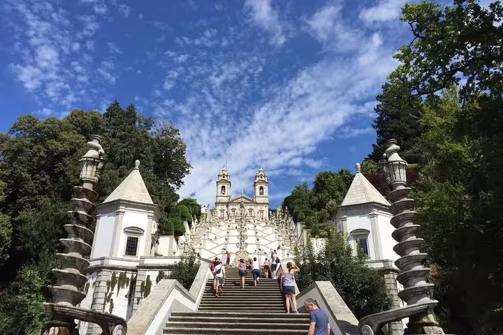 Visitors climbing the iconic staircase of Bom Jesus do Monte in Braga, surrounded by lush greenery and clear skies.