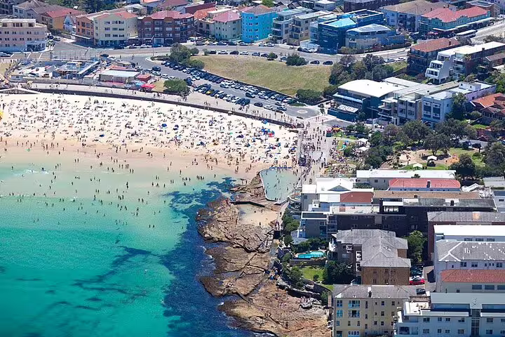 Aerial view of crowded Bondi Beach shoreline with turquoise water, sandy beach, and surrounding urban buildings