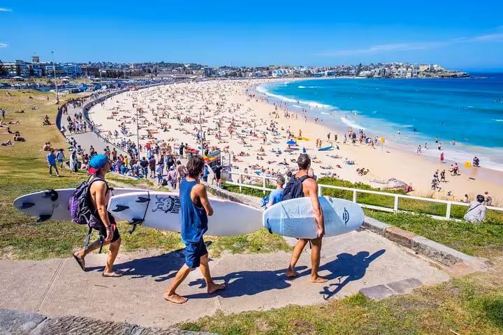 Surfers carrying boards towards Bondi Beach's golden sands and clear waters during a Sydney private tour.