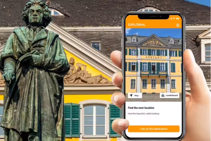 Smartphone app guiding Bonn scavenger hunt tour beside Beethoven statue and historic Postamt building