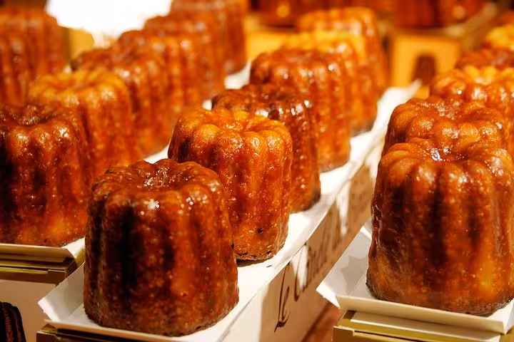 Rows of golden-brown canelés displayed enticingly on a Bordeaux food tour, showcasing rich French pastry delights.