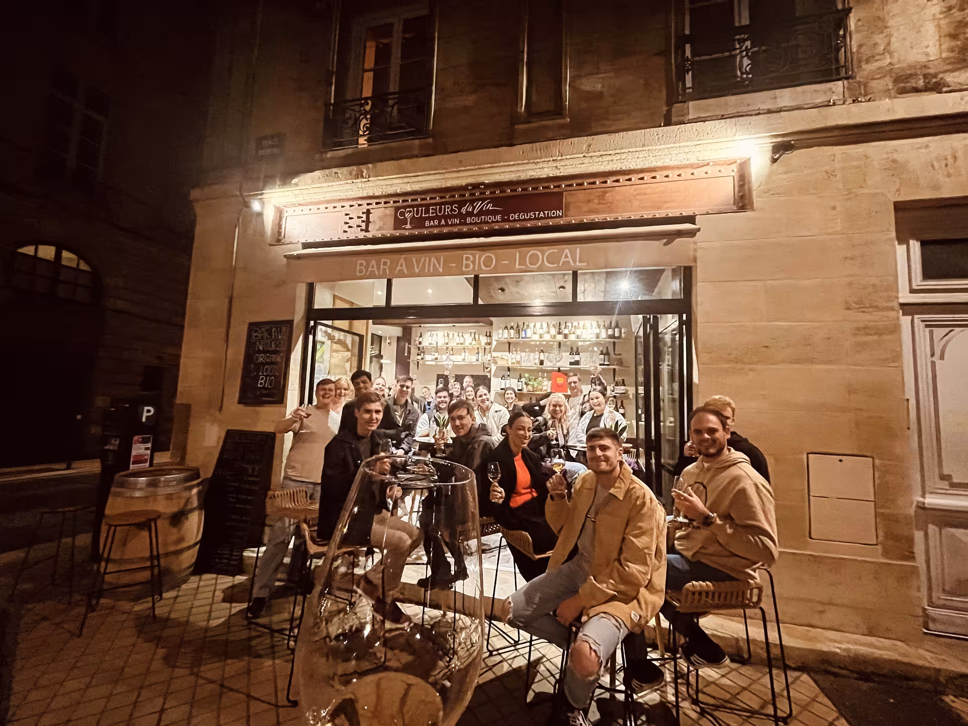 Group of wine lovers celebrating a Bordeaux natural wine blind tasting tour outside a local bio wine bar at night